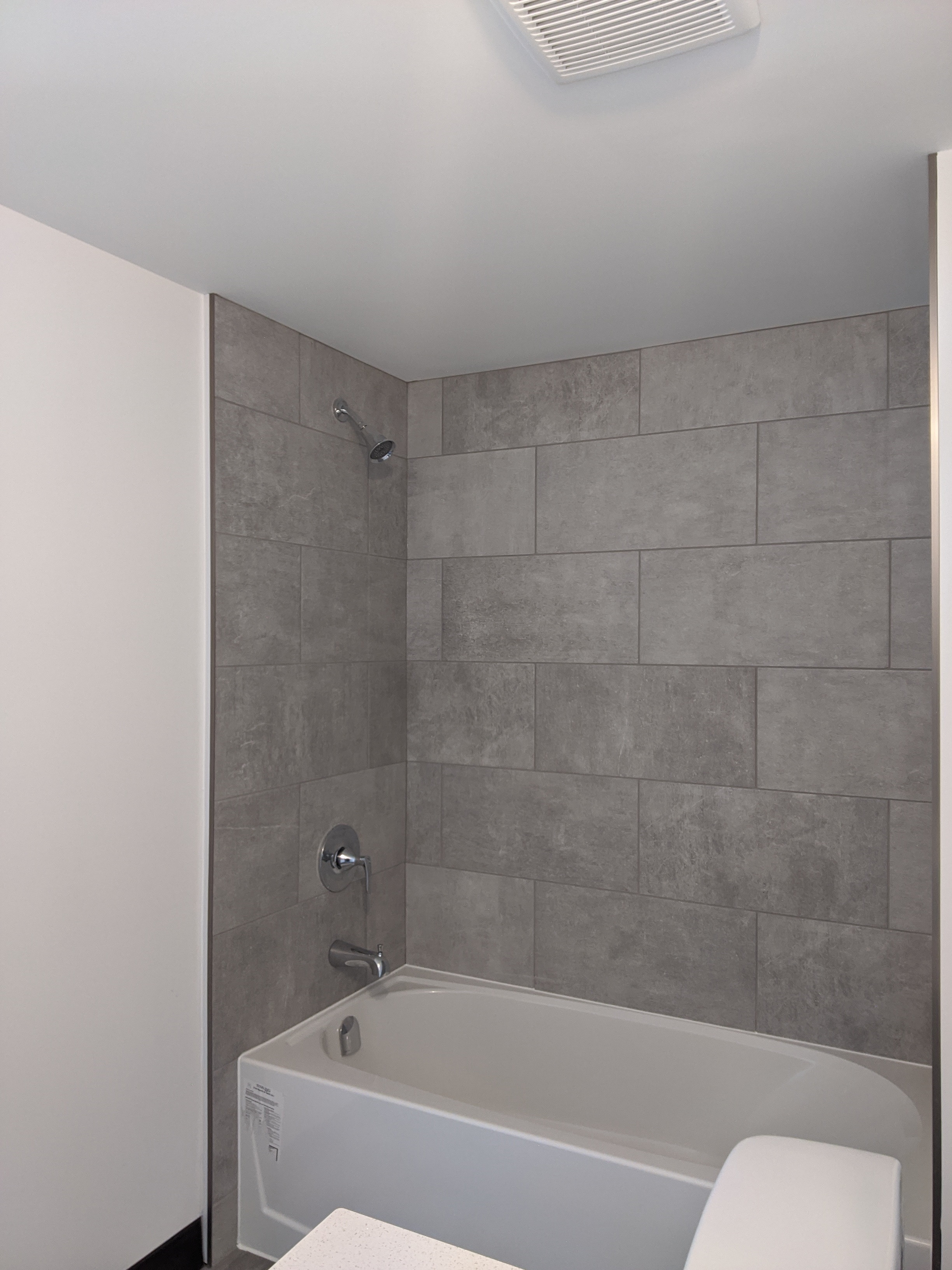 A white bathtub with a grey tile wall behind it.